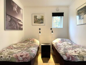 Un dormitorio con dos camas individuales, una mesita de noche, una ventana con vistas y dos lámparas de pared.
