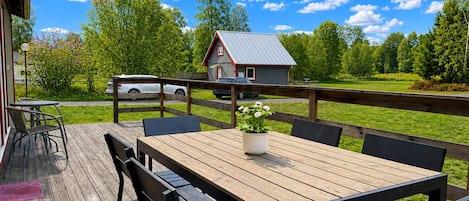 A wooden deck with a table and chairs, a small shed in the background, and a clear blue sky.