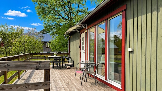 Une terrasse en bois avec des meubles d’extérieur, une porte vitrée et une vue sur la verdure.