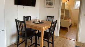 Un coin repas avec une table en bois et quatre chaises, un téléviseur à écran plat fixé au mur et un tableau encadré au-dessus de la table.