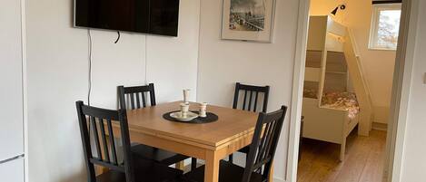 Un coin repas avec une table en bois et quatre chaises, un téléviseur à écran plat fixé au mur et un tableau encadré au-dessus de la table.