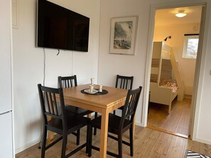 A dining area with a wooden table and four chairs, a flat-screen TV mounted on the wall, and a framed picture above the table. - 4 Star Holiday Home in Lottorp (Löttorp)