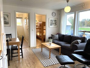 A modern living room with a sofa, a dining table, and a black leather chair. There is a wooden floor, a black and white rug, and a window with a view of the outdoors. - 4 Star Holiday Home in Lottorp (Löttorp)