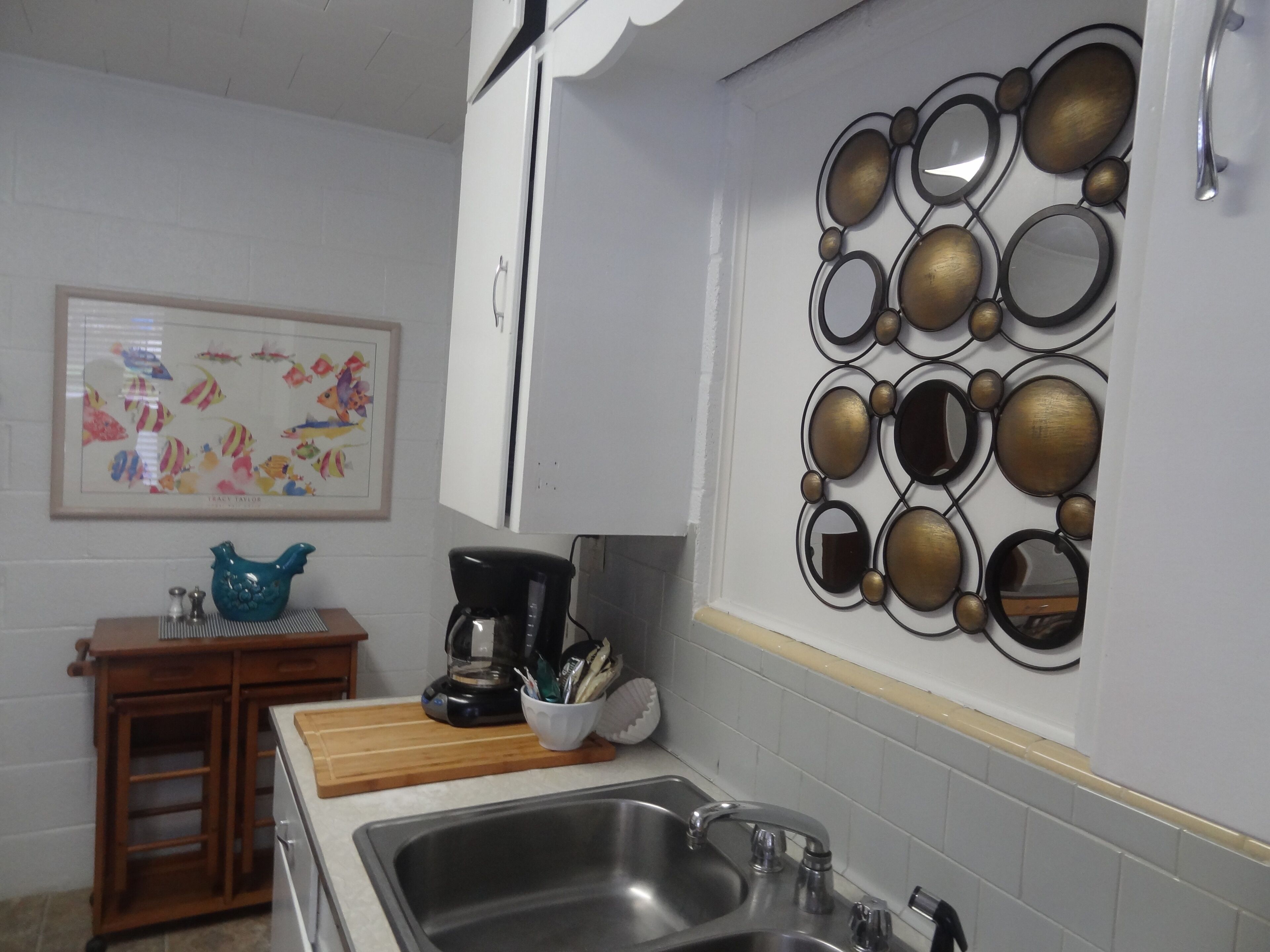 Een keuken met een spoelbak, een koffiezetapparaat, een decoratieve spiegelwand en een ingelijst schilderij aan de muur.