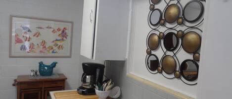 Een keuken met een spoelbak, een koffiezetapparaat, een decoratieve spiegelwand en een ingelijst schilderij aan de muur.