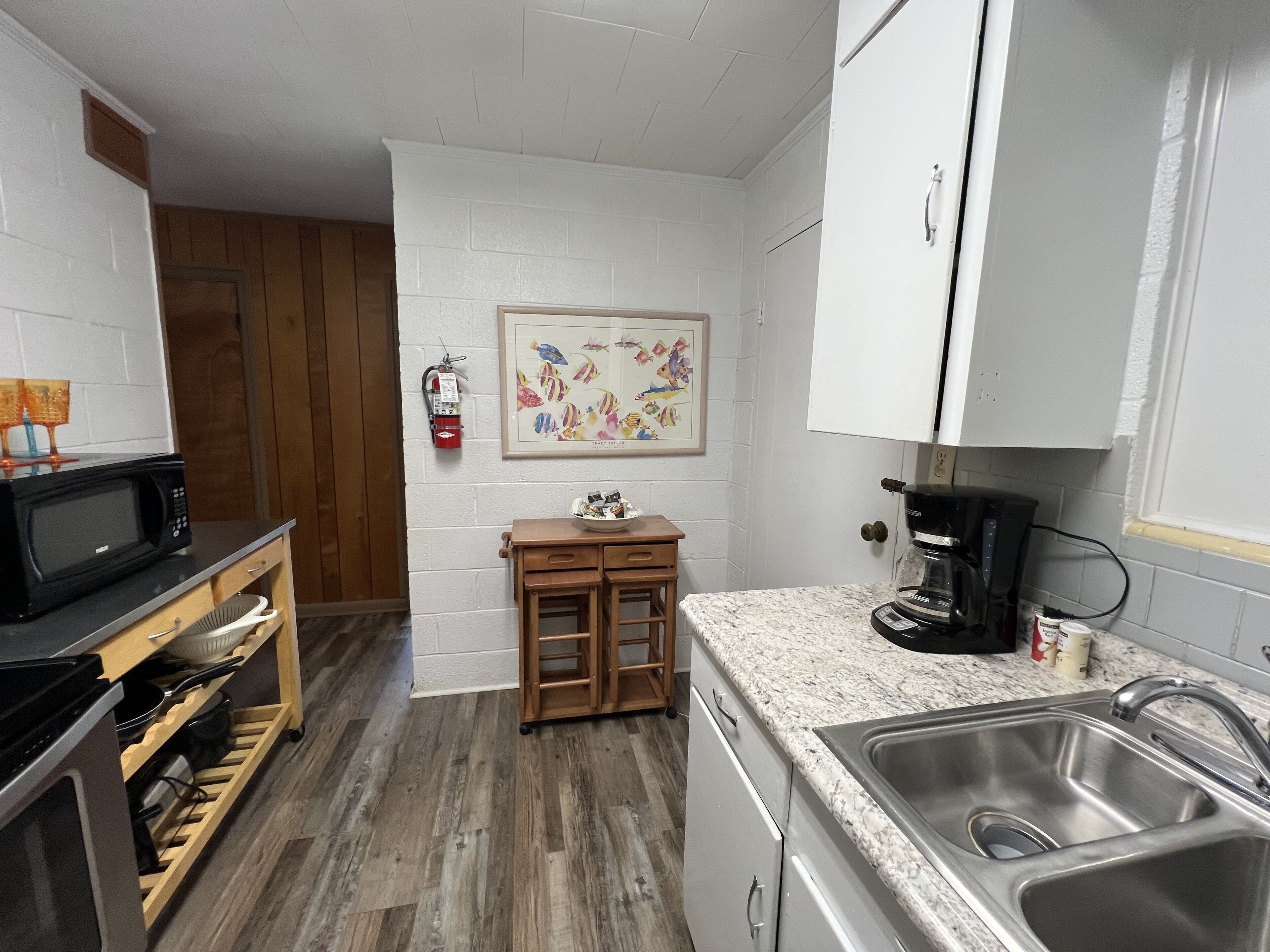A compact kitchen with white cabinets, a sink, a microwave, and a coffee maker.