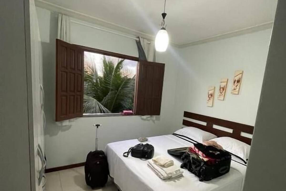 A small, clean room with a bed, a suitcase, and a window with curtains.