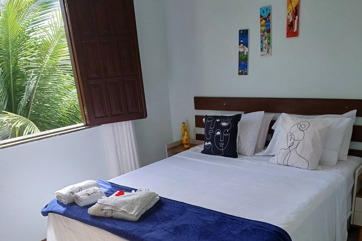 A hotel room with a bed, a window with curtains, a nightstand, and wall art.