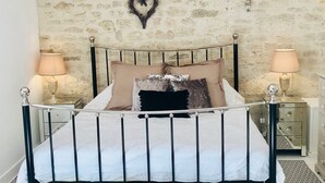 A bedroom with a stone wall, a chandelier, a bed with a metal frame, and two bedside tables with lamps.