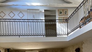 A spacious living area with a high ceiling, a balcony with a wrought iron railing, and a view of greenery outside.