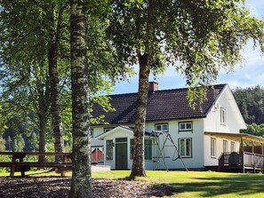 A two-story house with a green door, a swing set, and a wooden fence in a grassy area. - 11 Person Holiday Home in Hogsater (Högsäter)