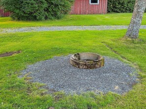Et cirkulært grusareal med en forhøjning i midten, omgivet af græs, med en rød bygning og et træ i baggrunden.