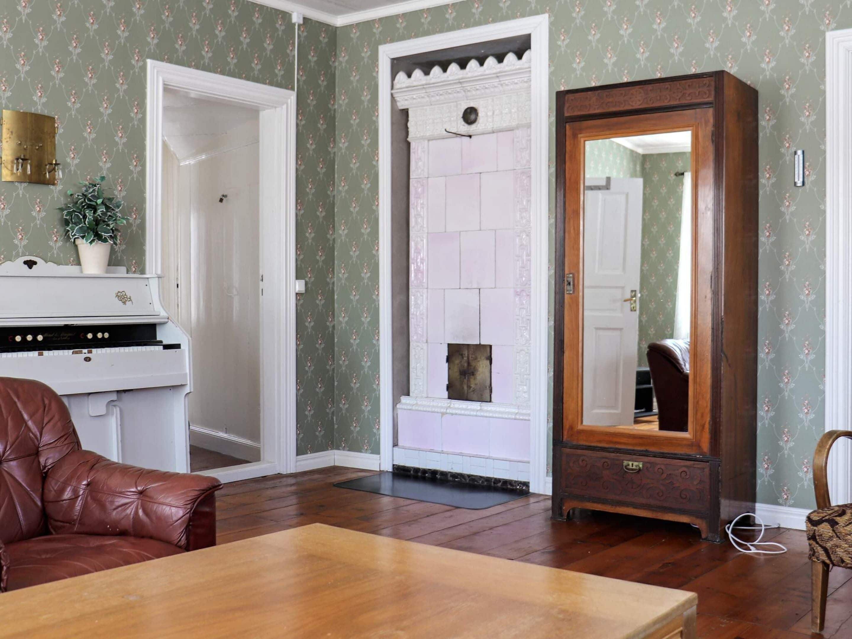 Una habitación con un piano, un sillón de cuero marrón, una mesa de madera y un espejo grande.