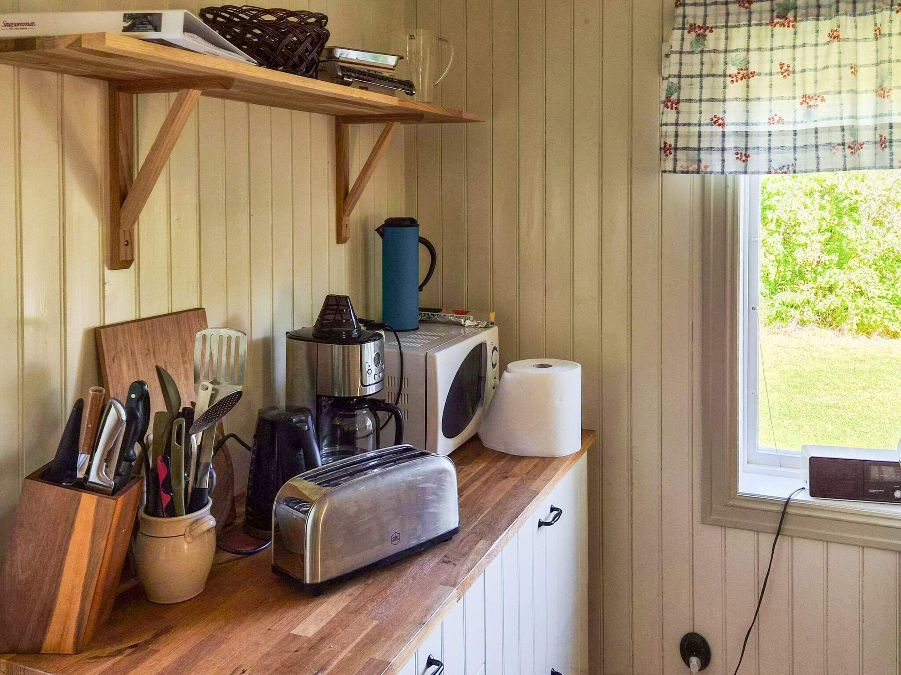 Une cuisine dotée d’un plan de travail en bois, d’un grille-pain, d’une bouilloire, d’un four à micro-ondes et d’une fenêtre donnant sur un paysage verdoyant.