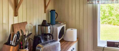 Une cuisine dotée d’un plan de travail en bois, d’un grille-pain, d’une bouilloire, d’un four à micro-ondes et d’une fenêtre donnant sur un paysage verdoyant.