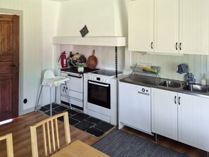 A compact kitchen with white cabinets, a stove, an oven, a sink, and a small dining area with a high chair. - 11 Person Holiday Home in Hogsater (Högsäter)
