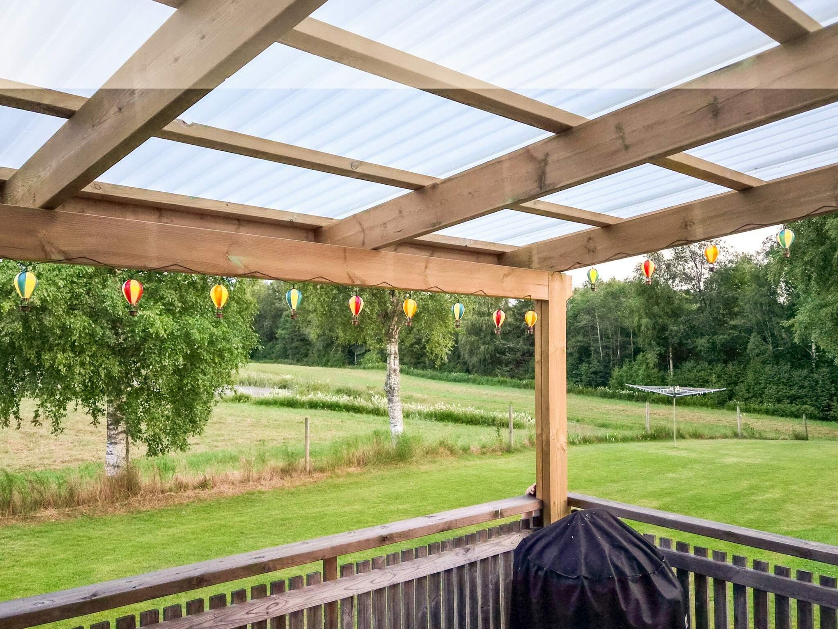 A wooden pergola with a transparent roof, a grassy landscape, and a tree in the background.