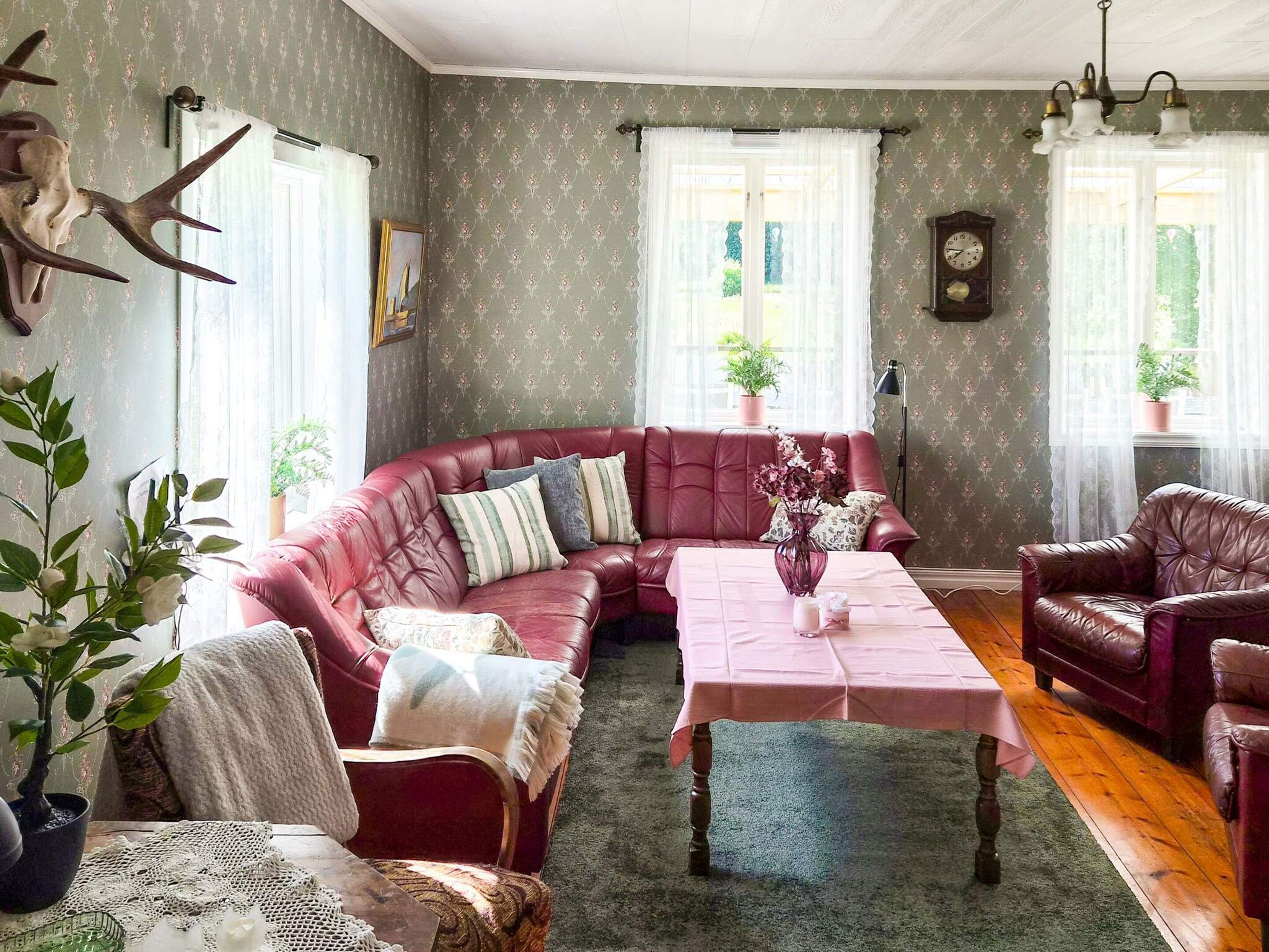 Una habitación con un sofá de cuero rojo, una mesa con un florero y un reloj en la pared.
