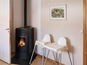 A room with a black wood-burning stove, two white chairs, and a framed painting on the wall. - 11 Person Holiday Home in Hogsater (Högsäter)