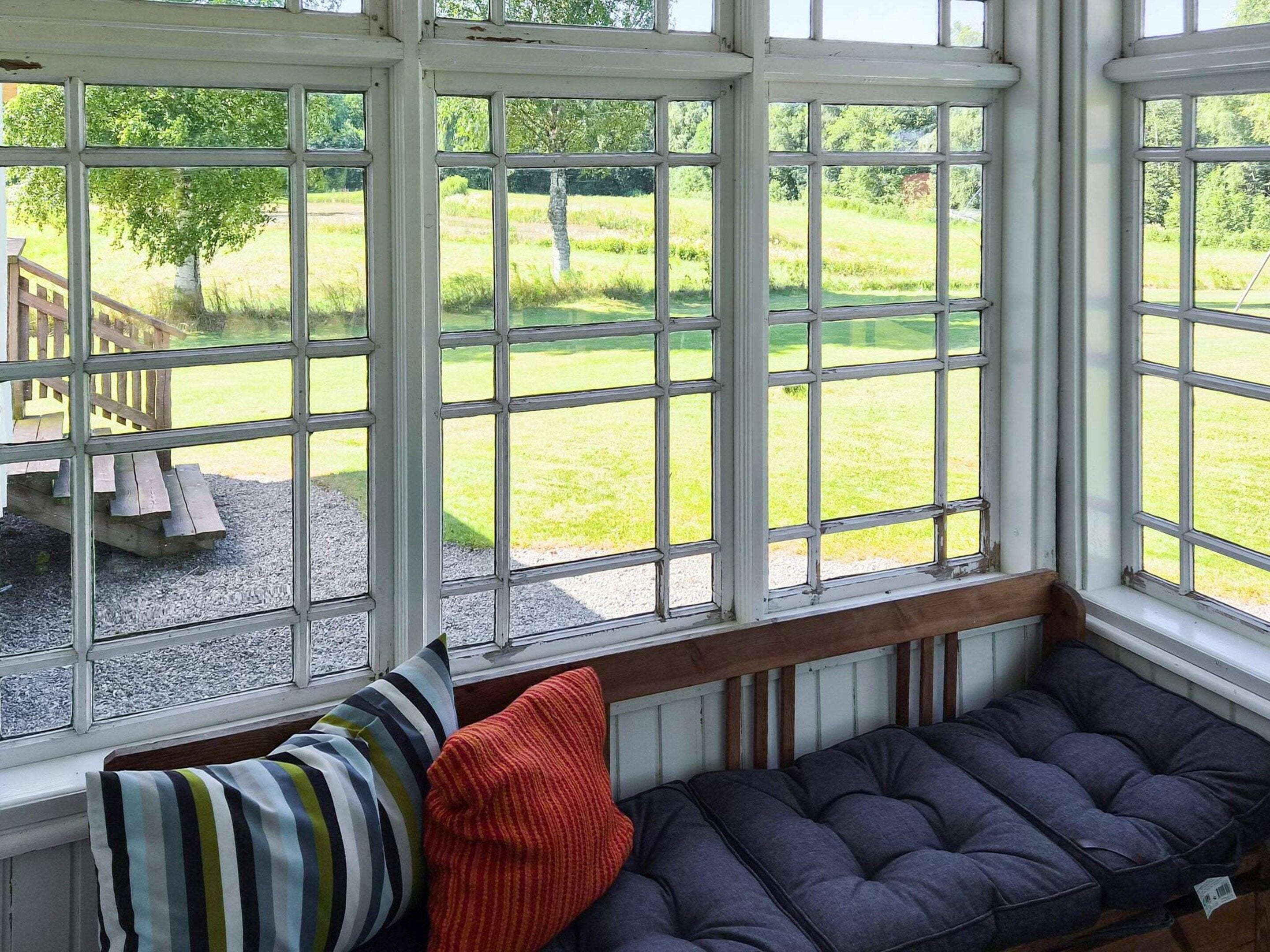 Habitación con un ventanal grande con vistas a un área verde, un banco con cojines y otro banco de madera afuera.