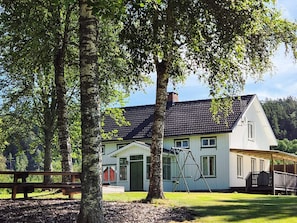 A two-story house with a black roof, surrounded by trees and a grassy yard. - 11 Person Holiday Home in Hogsater (Högsäter)