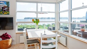 Un comedor con una mesa y sillas, un jarrón con girasoles y vista a un cuerpo de agua a través de amplias ventanas.