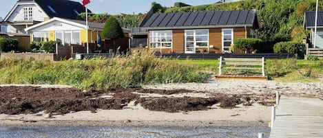 A coastal building with a flag, a wooden deck, and a sandy beach.