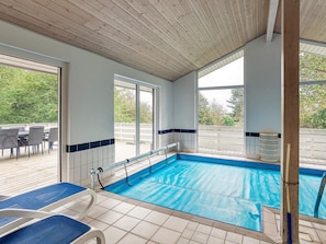 An indoor swimming pool with clear blue water, surrounded by white tiled walls and a wooden ceiling.