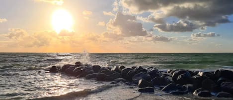 A beach with waves crashing against rocks and the sun setting in the background.