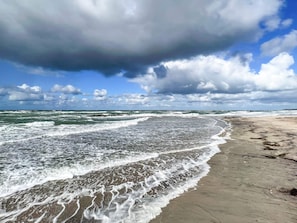 A beach with waves, a cloudy sky, and a sandy shore. - 12 Person Holiday Home in Hundested (Hundested)