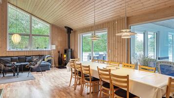 A spacious room with a long dining table, wooden chairs, a sofa, and a large window.