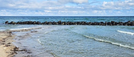 Una playa con agua cristalina, un rompeolas rocoso y una orilla arenosa.