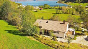 Una casa con techo de tejas, un balcón con mobiliario exterior y vista a un lago y montañas al fondo.