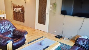 Una sala de estar con dos sofás de cuero, una mesa de centro de madera, un televisor montado en la pared y una puerta con panel texturizado.