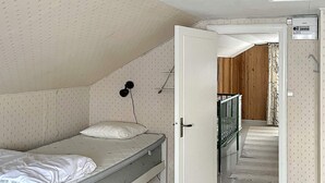 Habitación con cama individual, piso de madera, puerta blanca y mesita de noche pequeña.