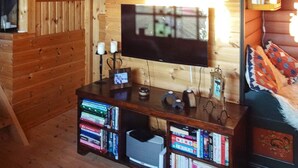 Ett mysigt rum med träinredning, en väggmonterad tv, en bokhylla med diverse föremål och en mönstrad pläd på en soffa.
