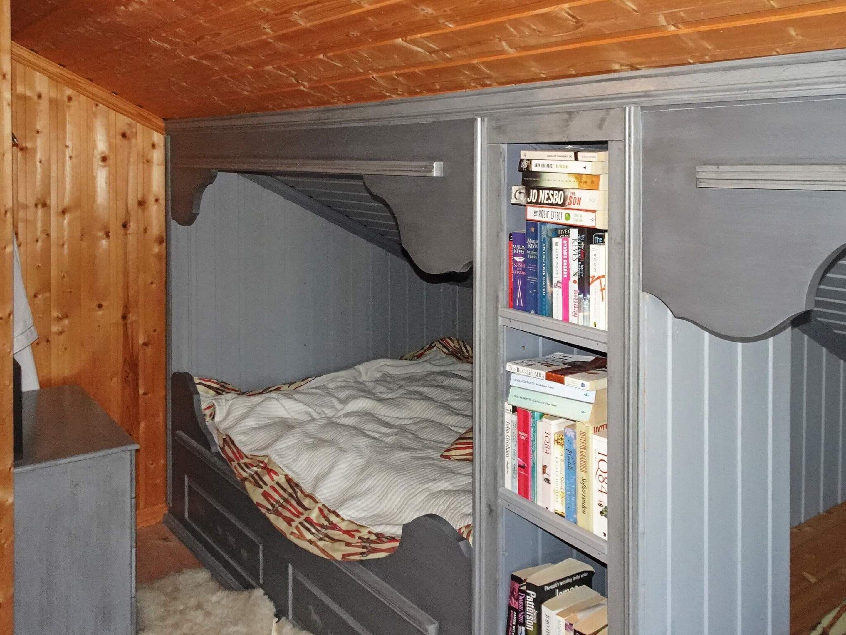 A bedroom with a bunk bed, a bookshelf filled with books, and a wooden ceiling.