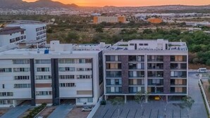 Un moderno edificio de apartamentos con varios pisos y balcones, rodeado por un paisaje desértico y montañas al fondo.