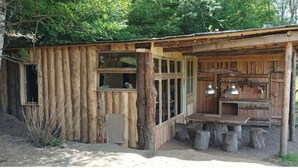 A rustic wooden cabin with a large window, a wooden table, and a bench.