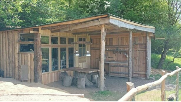 A rustic wooden cabin with a covered porch, large windows, and a small table.