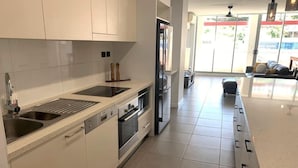 Una cocina moderna con armarios blancos, electrodomésticos de acero inoxidable y un amplio ventanal que proporciona luz natural.