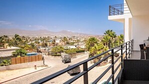 Un balcón con vista a un paisaje urbano, que incluye palmeras y una cadena montañosa distante.
