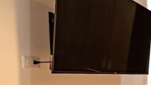 Un televisor montado en la pared en una habitación con pared lisa, un enchufe y suelo de madera.