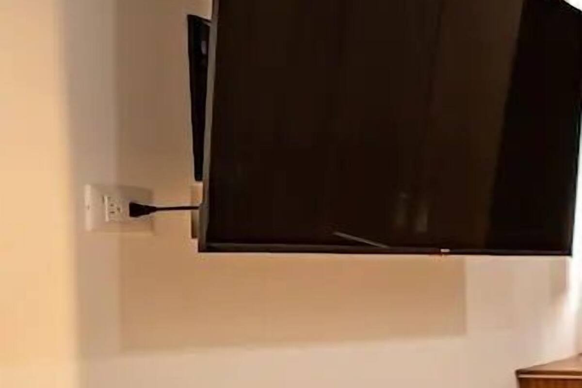 Un televisor montado en la pared en una habitación con pared lisa, un enchufe y suelo de madera.