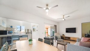A modern living room with a dining area, a kitchen, and a TV mounted on the wall.