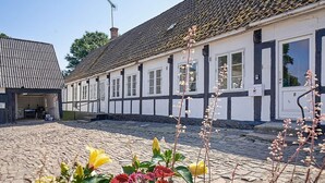 En traditionell byggnad med korsvirkesfasad, en innergård med kullerstenar, en liten intilliggande byggnad och en klar himmel.