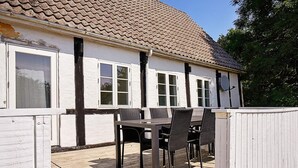 Ett hus med ett tak täckt av tegelpannor, vita ytterväggar och en träveranda med ett bord och stolar.