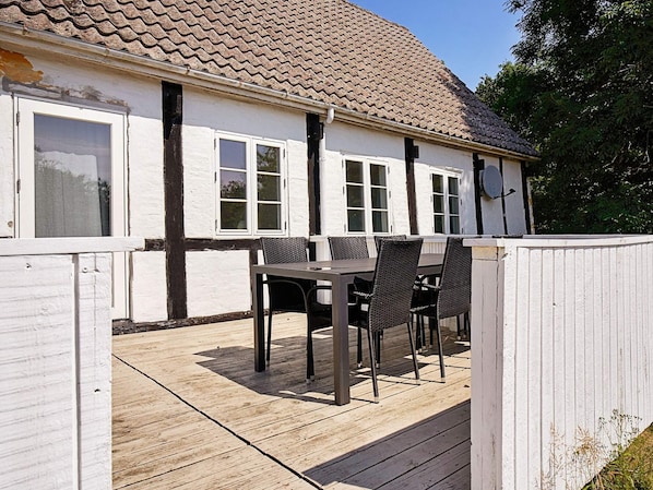 A house with a tiled roof, white exterior walls, and a wooden deck with a table and chairs.