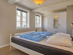 A bedroom with two beds, large windows, a wardrobe, and a ceiling light.