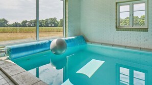 A swimming pool with a blue edge, a white brick wall, and a window overlooking a field. - 6 Person Holiday Home in Aakirkeby (Akirkeby)